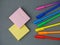 Scattered colored bright rainbow pens, yellow and pink square sticky paper sheets lying on grey background