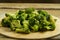 Scattered frozen broccoli on a round wooden board.