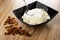 Scattered raisin, spoon in black bowl with grainy cottage cheese and sour cream on wooden table