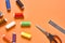 Scattered sewing accessories metal ruler, scissors and spools with colorful threads on orange tailors desk in workshop. Space for