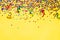 Scattered star shaped colorful glittering confetti and ribbons over yellow background. Copy space.