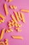 Scattered variety of uncooked golden wheat pasta on minimal pink background
