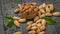 Scattered on a wooden table are unpeeled almonds and a wooden bowl with peeled almonds