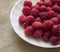 A scattering of fresh wild raspberries lying on a white plate. Close-up