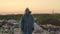 Scavenger wearing a gas mask and some garbage clothing, standing in the middle of an enormous dump located in the middle of a