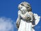 Scene in a cemetery: close-up of an old stone statue of a little angel with the hands clasped, praying.