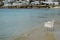 Scene of empty chair in white rattan sitting on sand beach with soft wave in clear sea water and white building on sea bank