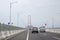 Scene of the famous Suramadu Bridge and its red suspension steel cables with cars and lamp post on road and cloudy sky background.