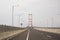 Scene of the famous Suramadu Bridge and its red suspension steel cables with cars and lamp post on road and cloudy sky background.