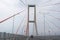 Scene of the famous Suramadu Bridge and its red suspension steel cables with cars on road and cloudy sky background.