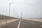 Scene of the famous Suramadu Bridge and its red suspension steel cables with lamp post on road and cloudy sky background.