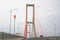 Scene of the famous Suramadu Bridge and its red suspension steel cables with lamp post on road and cloudy sky background.