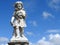 Scene in a graveyard: close-up of an old stone statue of a little angel holding some flowers.