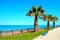 Scene in Porto Potenza Picena with palm trees, benches, paved walk, grass and sea