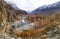 Scenery of blue turquoise river passing through colorful autumn in valley and snow capped mountains of Pakistan in cloudy day