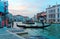 Scenery of romantic Venice at sunset, with view of a gondolier steering his ferry gondola by a pier, a vaporetto waterbus