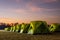 Scenery of rows of green canvas camping tents with floodlights installed on the lawn