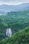 Scenery top view of beautiful waterfall in tropical forest, fresh mist, wild flowers with green mountains in rainy day. Khlong Lan
