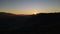 Scenic aerial view of the sunset over the mountains range, drone flies slowly backwards down and the sun hides behind
