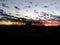 Scenic background. Orange, yellow, red and grey scattered clouds sunset above the silhouette of large trees and farm landscape