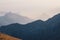 Scenic dawn mountain landscape with light fog in valley among mountains silhouettes under cloudy sky. Vivid sunset or sunrise