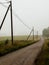 Scenic dirt road meandering through lush grass and tall telephone poles shrouded in a peaceful fog