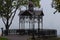 Scenic foggy landscape of autumn park with viewing platform. Beautiful metal arbor with wooden benches.