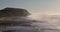 A scenic footage of a misty sandy beach with crashing waves along majestic cliffs under a beautiful blue sky