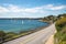 scenic highway running alongside a bay, with sailboats and seagulls in the background