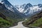 scenic highway winding through towering mountains, with snow-capped peaks visible in the background