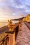 scenic landscape of morning sunrise on sea embarkment with road and sidewalk, fence with decorations of cactuses