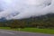 Scenic landscape photo of Slovenia. Beautiful green meadow under mountain which shrouded by sick fog