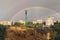Scenic landscape view of the city after rain. Double rainbow against a cloudy sky. Construction site with high crane in big city