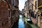 Scenic narrow canal with ancient buildings with potted plants in Venice, Italy