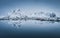 Scenic panorama of snow covered mountain range reflected in cold waters of arctic sea