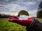 A scenic portrait of a glass lens ball resting on a red glove on a persons hand reflecting the up side down image of the meadow