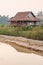 Scenic rural of vietnam at sunset, old wooden house, brown earthenware roof, pool foreground, forest and mountains backgrounds.