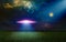 Scenic sci-fi image - ufo inspect green grass field with bright spotlight in dark night sky. Nebula and full moon in starry sky