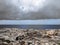 Scenic view of a coastline with rock pools on the edge of a limestone beach with bright blue calm summer sea dark clouds