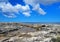 Scenic view of a coastline with rock pools on the edge of a limestone beach with bright blue calm summer sea and sunlit clouds