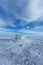 An scenic view of a frozen moutain summit with huge rocky trig point in the winter under a majestic blue sky and some white clouds