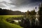 Scenic view at a golf course near a lake under a gloomy sky background