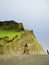 Scenic view of green cliffs on a black rocky shore on a cloudy day