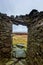 A scenic view from inside a stony mountain shelter in ruin under a grey stormy sky