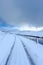 An scenic view of a moutain range in the winter with snowy slope and aqueduct under a majestic blue sky and some white clouds