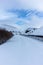 An scenic view of a moutain range in the winter with snowy slope and aqueduct under a majestic blue sky and some white clouds