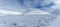 An scenic view of a moutain range in the winter with snowy slope and lake under a majestic blue sky and some white clouds