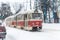 Scenic view of old vintage retro tram driving snowy city streets with traffic at heavy snowfall blizzard on cold winter