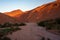 Scenic view on red and orange mountains against blue sky during sunset, dry riverbed in foreground, Morocco