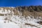 A scenic view of a rocky mountain cliff with some snow under a majestic blue sky